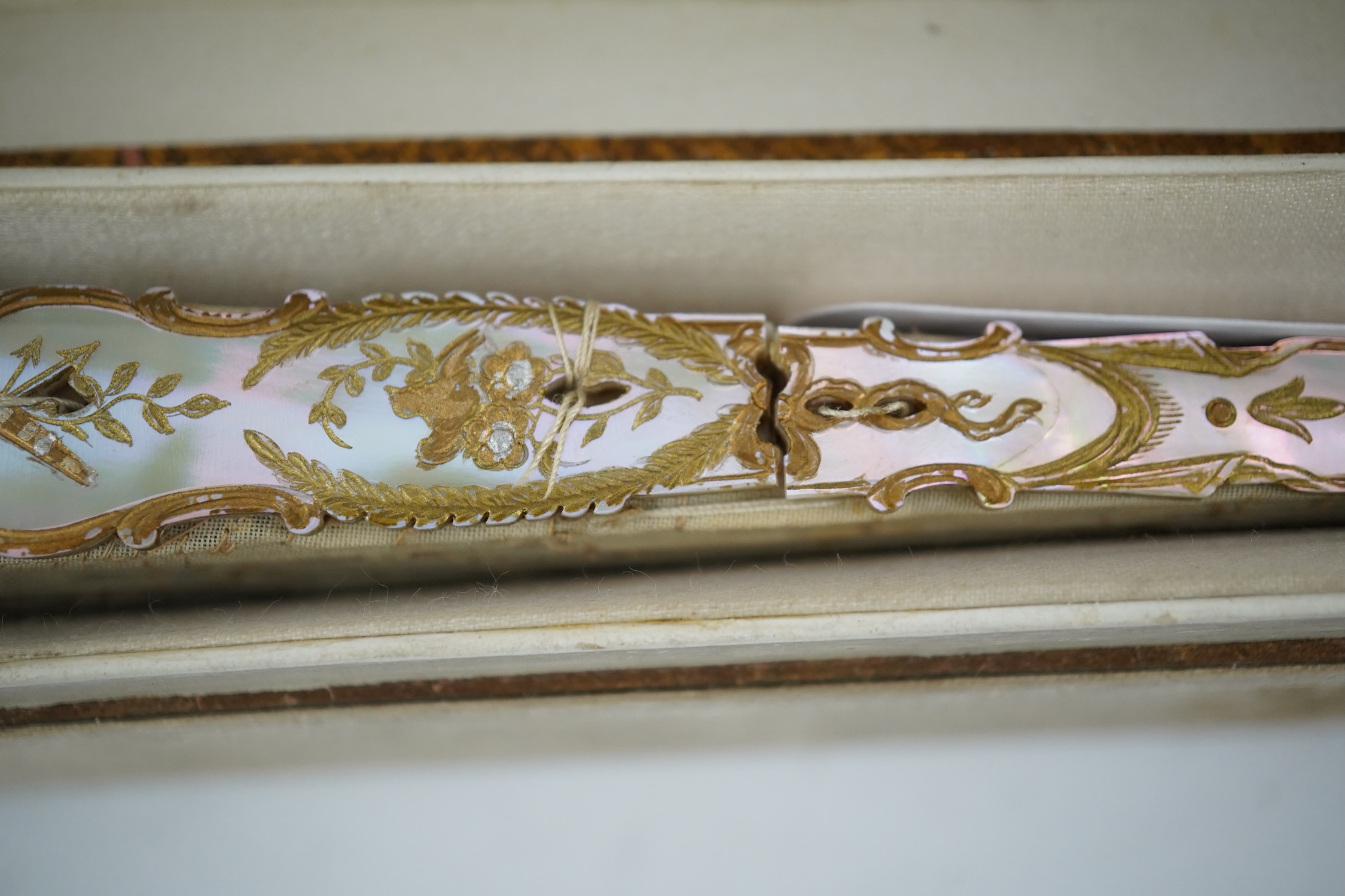 Three French fans: a mother of pearl and sequin fan boxed, a painted silk, feather and bone fan and a gilt decorated bone figural paper fan, the two bone fans having gilt mirrored mounts on the guards, figural paper fan